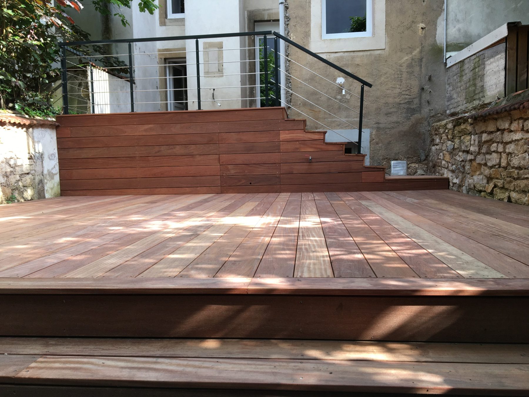Grande terrasse en bois exotique et escalier habillé de lames dans une cour